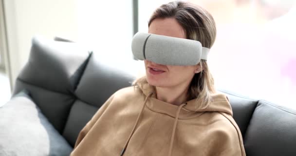若い女性は 睡眠のための仮想マスク クローズアップ 増加した外観を持つソファの上に座っています リラクゼーション装置 — ストック動画