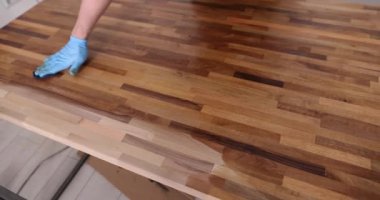 Katılımcının eli ahşap yüzeyi özel bir ilaçla cilalıyor, yakın plan. Ahşap ustası çalışıyor