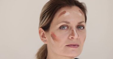 Yüzünde kozmetik ürünleri olan genç bir kadın. Yakın plan. Makyaj eğitimi, krem seçimi, yavaş çekim