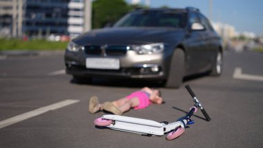 Küçük kız, arabayla çarpıştıktan sonra asfaltta scooterla yatıyor. Yol kavramında çocuğa vurmak