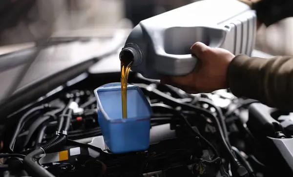 Master repairman pouring motor oil into car engine closeup. Engine oil change center concept