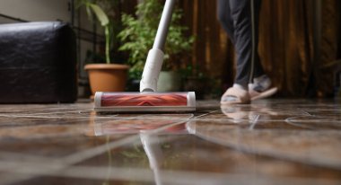 Cordless vacuum cleaner with turbo brush cleans tiles in living room. Modern home cleaning technology concept