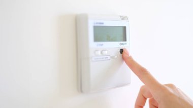 Wall mounted digital climate control and home thermostat. Female fingers set comfortable degrees of temperature adjustment in living room or hotel closeup