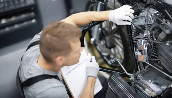 Car mechanic inspects motorcycle breakdowns in car repair shop. Motorcycle maintenance and repair concept