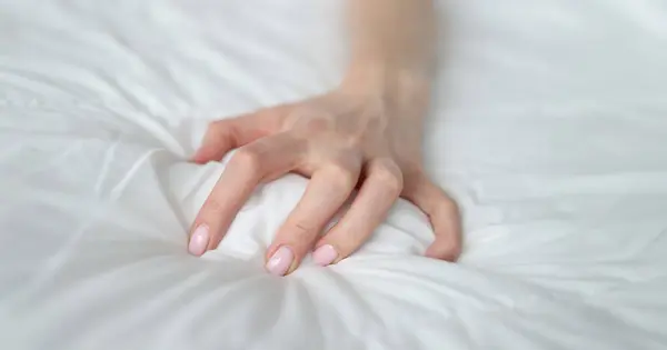 Woman hand tightly grips white sheet on bed. Nightmares and temper tantrums in the morning