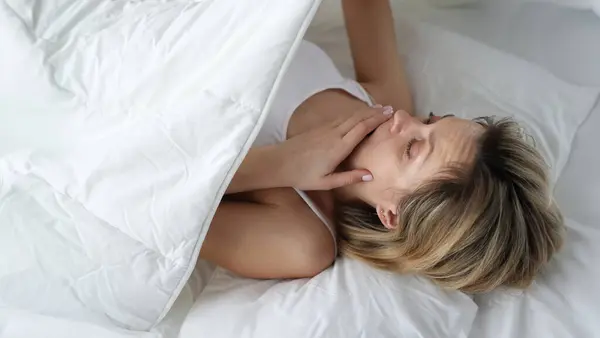 Woman looks in shock under covers in bed. Bedwetting in women concept