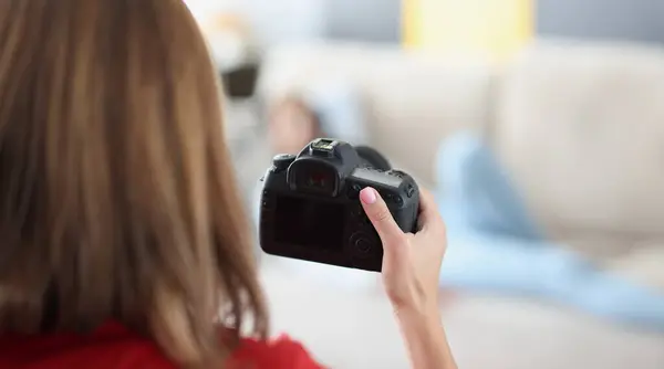 Woman holds professional black camera in hands and photographs model at home. Working photographer and stocker concept
