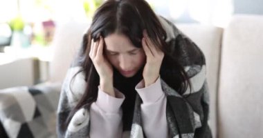 Başı ağrıyan ve şakakları olan bir kadın kanepede oturuyor. Kafa konseptinde ağrı için masaj