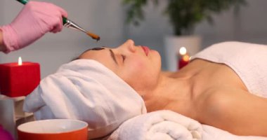 Güzellik salonu 4K filminde kadın müşterinin yüzüne siyah kilden maske takan bir güzellik uzmanı. Spa tedavisi kavramı