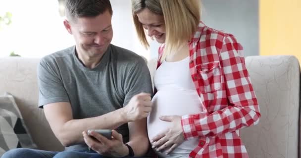夫婦は携帯電話を見て妊娠中の妻の腹に4K動画を置きます 将来の親の概念の幸福 — ストック動画