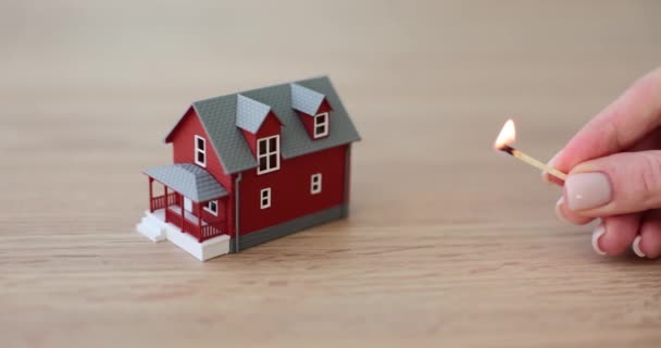 女人的手把点燃的火柴带到木制桌子上的小房子模型上 家庭纵火保险的概念 红色墙壁慢动作公寓的缩微胶片 — 图库视频影像