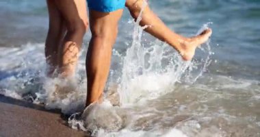 Sahilde insanlar deniz dalgalarını çıplak ayakla tekmeliyor. Aktif turistler sahilde günün tadını çıkarırlar. Yavaş çekimde çiftler tatil ve eğlence.