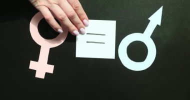 Kadın eli, siyah arka planda kadın ve erkek kağıt sembolleri arasına denklem işareti koyar. Çağdaş toplumda eşit haklar ve cinsiyet fırsatları