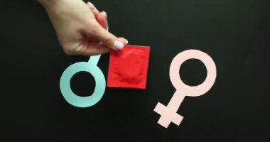 Kadın eli siyah arka planda erkek ve kadın sembollerine prezervatif paketi koyar. Cinsel yolla bulaşan hastalıklardan korunma. İstenmeyen hamileliğin önlenmesi