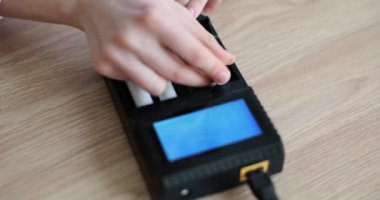 Kadın batarya için hücreleri tahta masadaki şarj cihazına yerleştiriyor. Güç elementi yeniden yükleniyor. Kadın ağır çekimde elektronik alet kullanıyor.