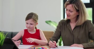 Pozitif kadın küçük kıza tablet kullanarak ödevlerini yapmasına yardım ediyor. Öğretmen, okul kızına oturma odasında ağır çekimde anlatılan şeyleri anlatıyor.