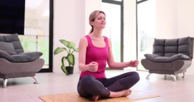 Kadın ellerini nilüfer poz vererek dua hareketlerine sokuyor modern evdeki paspasın üzerinde oturuyor. Ev rahatlama konsepti. Spor giyim sektöründeki kadın yoga egzersizlerini yavaş çekimde seviyor.
