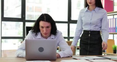 Sinirli erkek yönetici dizüstü bilgisayarda çalışıyor ve kızgın bir şekilde bayan meslektaşına yaklaşmak için ayrılmak istiyor. Meşgul patron masa başında oturan çalışanı kovalıyor.