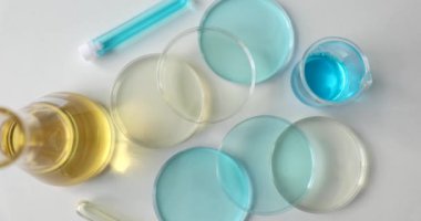 Masada renkli bir sıvı bulunan profesyonel bir laboratuvar bardağı. Test tüplü cam şişe ve sarı ve mavi reaksiyonlu Petri kabı.