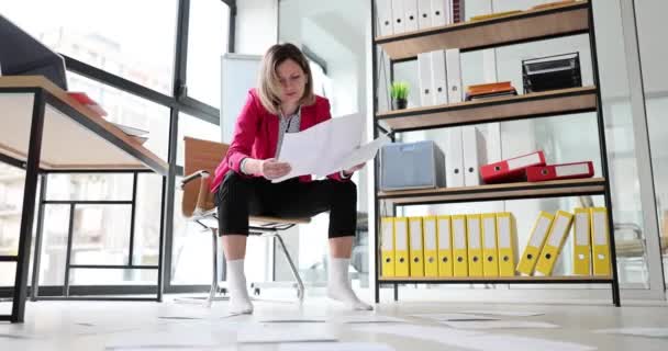 穿着袜子的女员工将数据分散在地板上的文件单进行分类 以方便操作 坐在办公室椅子上的女工检查商业文件 — 图库视频影像