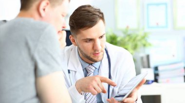 Parmaklarıyla cihaza işaret eden konsantre doktor portresi. Hasta, doktor tavsiyelerini dikkatle dinliyor. Tıbbi tedavi konsepti. Bulanık arkaplan