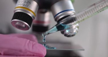 Bilim adamı kimyager, mikroskobun önünde cam parçasına mavi sıvı döküyor. Yakın çekim 4K film ağır çekimde. Aşı geliştirme kavramı