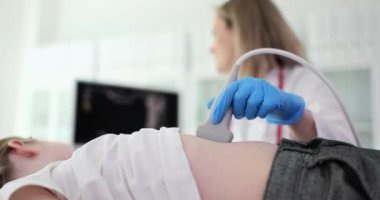 Doktor tarayıcı kullanan bir kız için ultrasonda karın boşluğu yapar. Doktor ekrana bakarken hastanın karnında ultrason sondası çalıştırıyor.