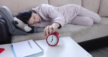 Genç kadın kanepede uyuyor ve çalar saati kapatıyor. Uyku yorgunluğu ve depresyon kavramı