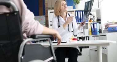Tekerlekli sandalyedeki kadın ortopedik doktorla buluşup röntgenleri tartışıyor. Sırt yaralanması konsepti olan engelli hasta danışmanlığı