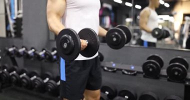 Güçlü adam modern spor salonunda ağır dambılları kaldırır. Motive olmuş sporcu kol kaslarını yavaş çekimde şişirmek için ağırlıkla etkili egzersiz yapar.
