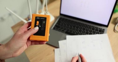 Ofisteki şebeke kontrolü için LAN hız testçisi kadının elinde. Kullanıcı evde yavaş çekimde modern aygıt kullanarak internet bağlantısını ve telefon kablosunu kontrol ediyor