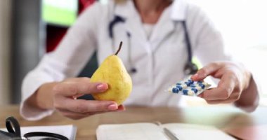 Kadın doktor klinikteki masada taze armut ve el hapları sunuyor. Profesyonel beslenme uzmanı taze meyve ve diyet takviyeleri tavsiye ediyor