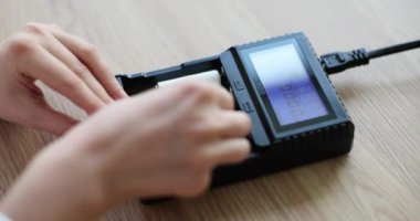 Kadın elleri şarj aletine batarya takmak için hücreleri yerleştiriyor. Ahşap masadaki batarya gücünü arttırmak için bir cihaz. Elektronik aygıtların yavaş çekimde çalışması için destek