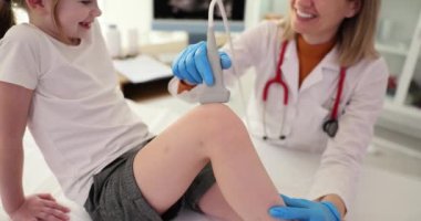 Doktor, çocuk kliniğinde diz eklemini ultrasonla muayene ediyor. Çocuklarda kemik hastalıklarının teşhisi ve menisküs ağrıları
