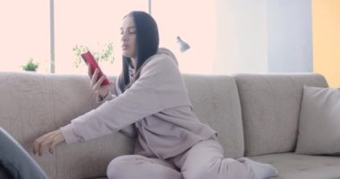 Woman sitting on couch with mobile phone in her hands 4k movie slow motion. Home leisure remote communication concept
