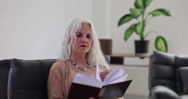 Gri saçlı yaşlı kadın evde ağır çekimde koltukta kitap okuyor. Yaşlı bayan oturma odasında ilginç edebiyattan hoşlanıyor.