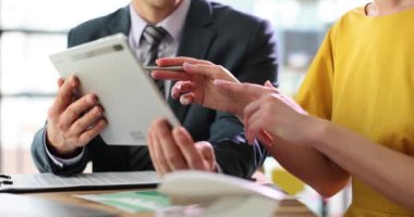 Kadın, meslektaşlarına görevlerini açıklıyor. Ofisteki tablet üzerinde veri gösteriyorlar. Müdür, iş yerindeki genç çalışanlara talimat veriyor.