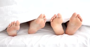 Çıplak ayaklı adam, sabahları yatakta yatan kadına dokunur. Çıplak ayaklı evli çift yatak odasında beyaz battaniyeden sarkıyor.