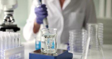 Laboratuvar asistanı ayrıntılı soruşturma için matarada su hazırlıyor. Kadın cam kaplamalı sıvıyı inceliyor. Yavaş çekimde girdap yapıyor.