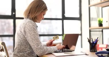 Sarışın kadın, iş yerindeki ağır çekimde kredi kartı ve laptop kullanarak internetten mal sipariş ediyor. Ofisteki internet servisinin parasını bayan ödüyor.