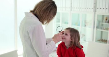 Kadın optometrist modern doktor muayenehanesinde küçük kız gözünü inceliyor. Gülümseyen liseli kız ağır çekimde uzman doktorla randevuda oturuyor.