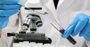 Laboratuvar çalışanı test tüpünden toprak alıyor ve mikroskop altına alıyor. İş üniformalı kişi toprak toprak elementlerini araştırır.