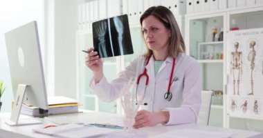 Tıp alanındaki kadın profesyonel hasta avuç içi kemiklerinin röntgen görüntülerine bakıyor. Üniformalı doktor yavaş çekimi dikkatlice inceliyor.