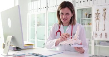 Steteskoplu kadın doktor el iskeletinden bahsediyor. Tıp alanında uzman hafif hastane ofisinde kol iskeleti sunuyor.