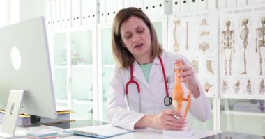 Üniformalı kadın doktor, hafif ofisteki iskelet üzerinde çalışmayı açıklıyor. Steteskop uzmanı, eklemlerin yavaş çekimde çalışması hakkında konuşuyor
