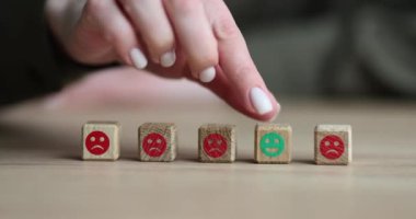 Kadın parmağı, bulanık arka planda negatif yüz ifadesi olan bloklara karşı yeşil pozitif emojili ahşap küpü hareket ettirir