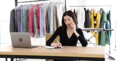 Esmer yönetici cep telefonuyla konuşur not defterinden sipariş puanı alır. Koyu renk elbiseli genç bir kadın ahşap masada kuru temizlemecide oturuyor.