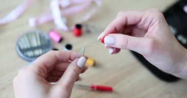 Bakımlı kadınlar ince iğneden ipliği iterek geçirirler. Çıplak manikür ipliği olan bir kadın, iplik iğnesine karşı masada iplik olan bir kadın.