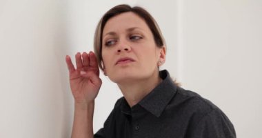 Katı saç stili olan kadın ofis duvarına yaslanmış kulak misafiri oluyor. Siyah gömlekli tatminsiz kadın dedikoduları yaymak için kelimeleri anlamaya çalışır.