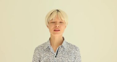 Klasik bluzlu genç bir kadın, onaylamak için başını sallıyor. Kısa sarı saçlı bayan, sarı duvarda ağır çekimde duran hareketleri onaylıyor.